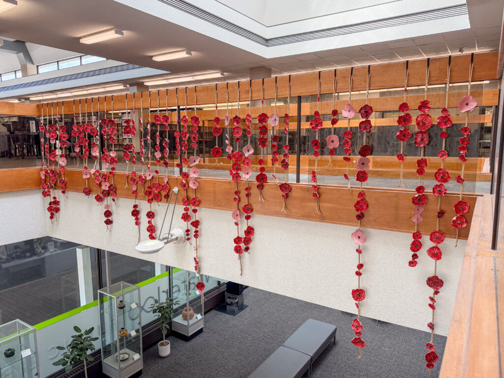 Rows of red poppy flowers made of ceramics and paper on strings hung from a railing at an atrium