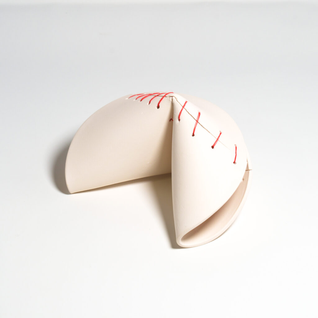 A large, broken ceramic fortune cookie mended together with red thread.