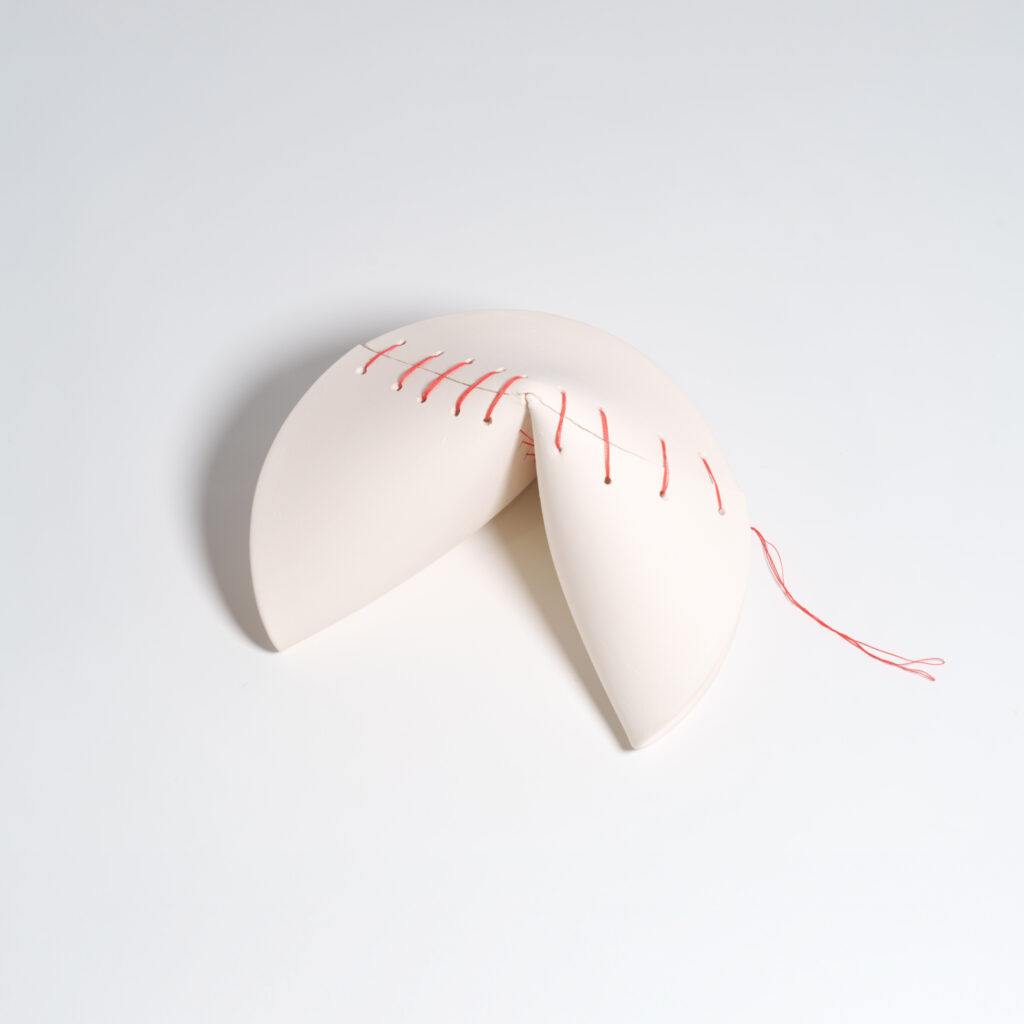 A large, broken ceramic fortune cookie mended together with red thread.