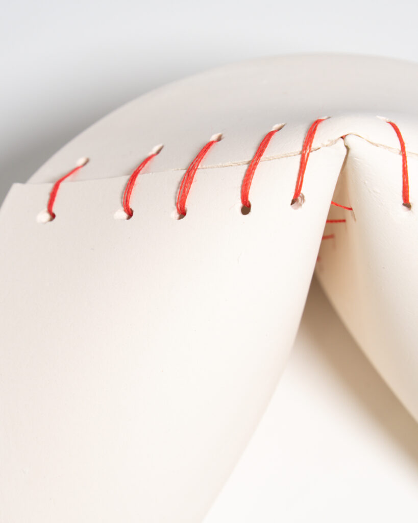 Details of a large, broken ceramic fortune cookie mended together with red thread.