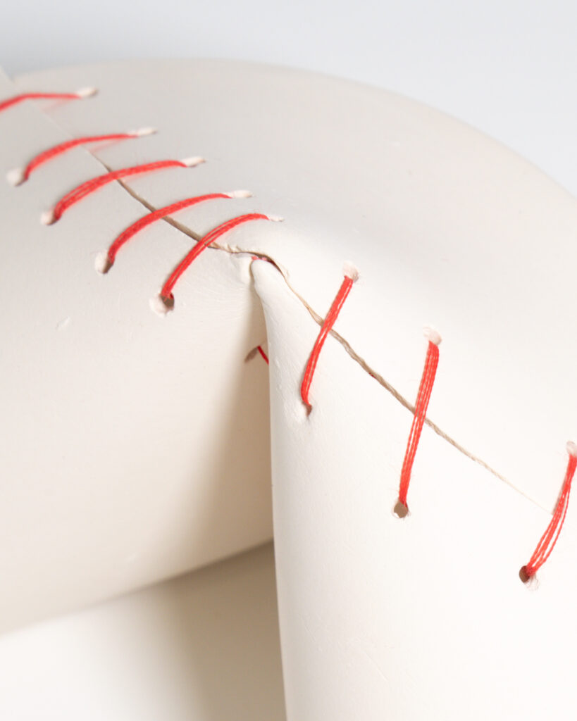 Details of a large, broken ceramic fortune cookie mended together with red thread.